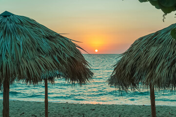 Beautiful sunset over the ocean with straw beach umbrellas and turquoise waters creating a relaxing vacation scene