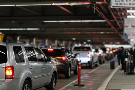 An airport terminal arrival pick-up area outside with a line of vehicles. blurred people are waiting with luggage. evening background with bokeh light effect