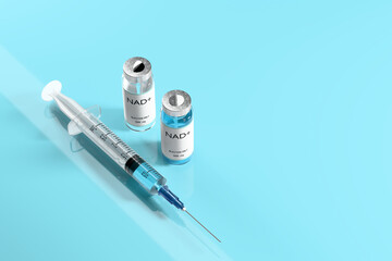 NAD+ solution in vials for injection and syringe on a blue glossy laboratory table. Concept of anti-aging therapy and life extension. 3d illustration, rendering. Copy space