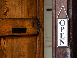 A wooden door slightly ajar with an OPEN sign hanging on it.