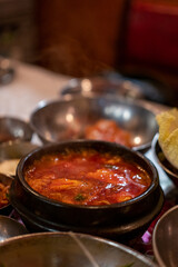 Kimchi Soup served in a bowl, with Korean side dishes served on the table