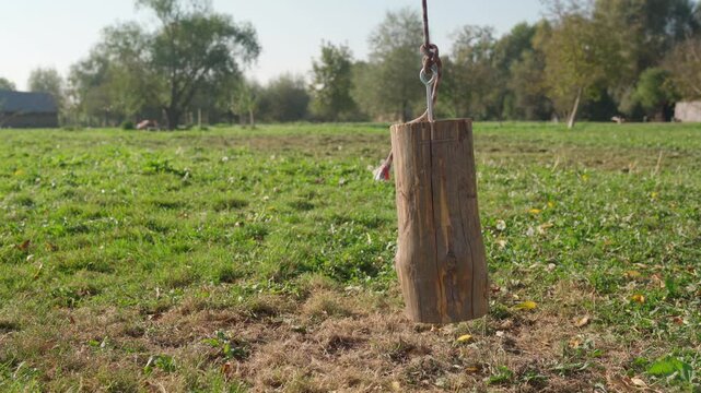 Wooden log hanging from a rope for ram, gently swaying over a green grassy field. Rustic outdoor setting.