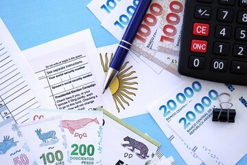 Argentine pesos money bills in big amount lies on table with pen, calculator, passport and tax forms