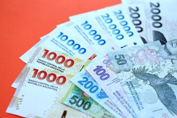 Argentine pesos money bills in big amount lies on red color table close up