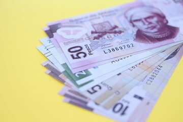 Mexican pesos money bills in big amount lies on yellow color table close up