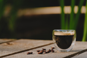 Double wall glass cup of espresso with plant filled pond in background