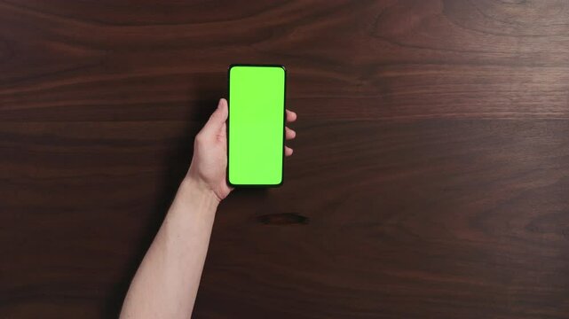 Top view man hand using smartphone with green screen over black walnut wood table