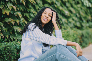A Joyful Young Woman Sitting Peacefully in Nature Surrounded by a Lush Greenery Background