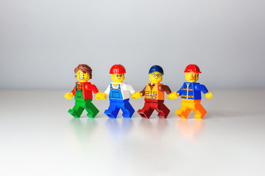 Tallinn, Harju, Estonia - 09.10.2021: Lego toy worker minifigures in colorful outfits and safety helmets holding hands and walking together. Concept of teamwork on a neutral background.