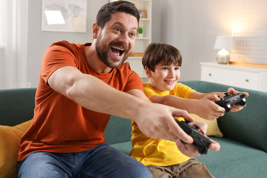 Happy father and his son playing video games on sofa in living room