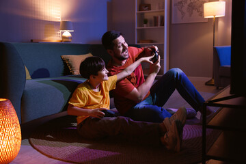 Happy father and his son playing video games on floor in living room at night