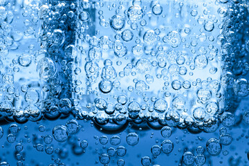 Soda water with bubbles and ice cubes as background, closeup