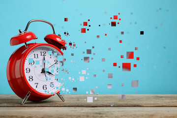 Alarm clock dissolving on wooden table against light blue background. Flow of time