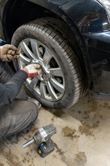 Seasonal Tire Change Service with an Automotive Technician Working on a Black Vehicle. Professional Using an Impact Wrench for Summer Wheel Installation
