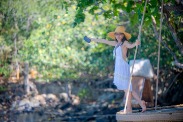 Woman tourist in dress play around on the wooden swing at the edge of the sea beach, enjoy moment of the woman in summer trip