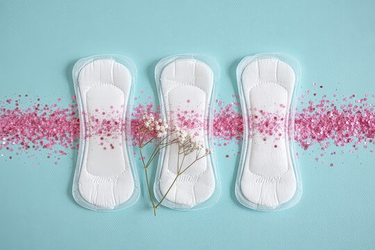 Female hygiene pads and pink glitter on blue background.