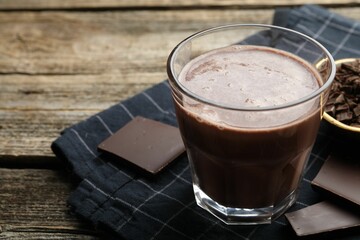 Tasty chocolate milk with shavings and pieces on wooden table, closeup. Space for text