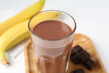 Tasty chocolate milk in glass, pieces and bananas on white table, closeup