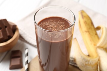 Tasty chocolate milk in glass, banana and pieces on table, closeup