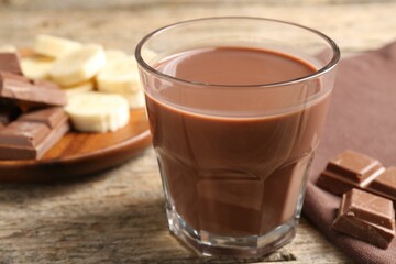 Tasty chocolate milk, pieces and banana on wooden table, closeup
