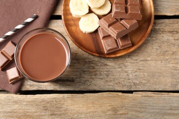 Tasty chocolate milk in glass, pieces and banana on wooden table, flat lay. Space for text