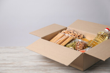 Different food products in box on wooden table against light background