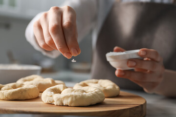 Woman adding sea salt onto uncooked pretzels at table indoors, closeup
