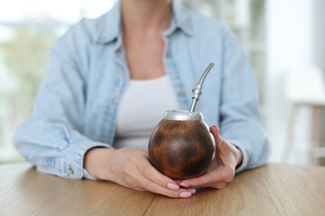 Woman with traditional yerba mate tea at table indoors, closeup