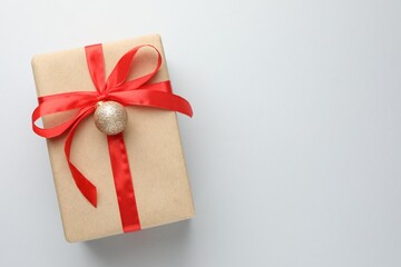 Gift wrapped in kraft paper with Christmas ball on light background, top view. Space for text