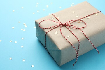 Gift wrapped in kraft paper and confetti on light blue background, closeup