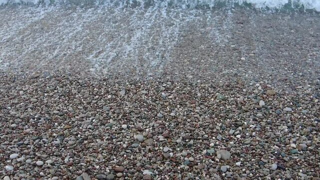 4K Top-down view of waves with sound on rocky beach in Antalya, Turkey. Overhead shot of Mediterranean sea waves washing over a textured pebble beach in Antalya, Turkey