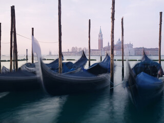 Long exposure photo of Gondolas moored near San Marco square at sunrise with a view at San Giorgio Maggiore Church at the background. Venice, Italy.
