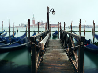 Long exposure photo of Gondolas moored near San Marco square at sunrise with a view at San Giorgio Maggiore Church at the background. Venice, Italy.