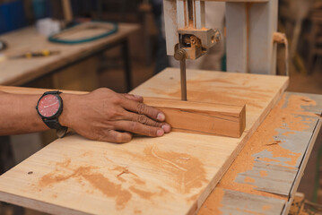 Worker guiding a wooden block through a bandsaw for precise cutting in a carpentry workshop, with...