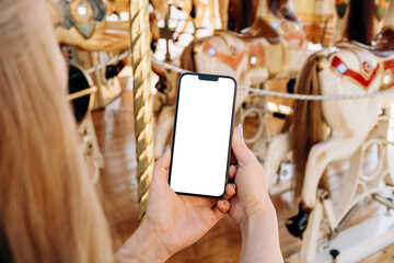 Mockup for  mobile app design and advertising, online marketing with woman's hand holding  smart phone on the background of a carousel with horses