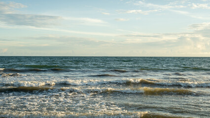 Fototapeta premium A tranquil scene featuring gentle ocean waves under a cloudy sky during sunset. Perfect for concepts of relaxation, nature beauty, and serene outdoor activities.