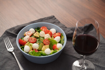 Salad with romaine, tomatoes and mozzarella in blue bowl with glass of red wine