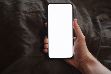 man hand holding phone with white screen over bed on background