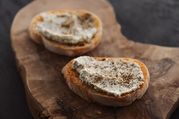 Ciabatta slices with cream cheese and herbs on olive wood board