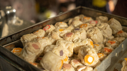 Close up of uncooked dim sum arranged in a metal tray, fresh handmade street food with various fillings, soft texture and savory appearance, Asian culinary preparation at local food market.