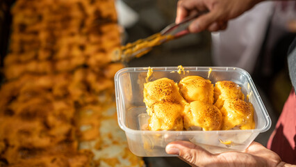 Delicious dim sum covered with melted cheese, freshly grilled and served in a plastic container,...