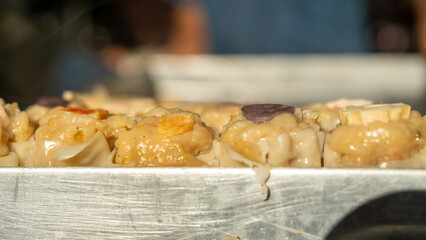 Close-up of steamed dim sum served on a metal tray, highlighting texture and savory fillings in soft natural light.