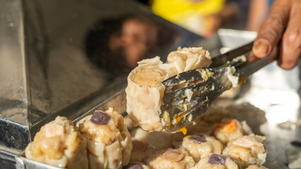 Close-up of a street vendor using tongs to serve freshly steamed dim sum in natural daylight,...
