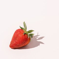 Ripe Strawberry with Shadow on Pale Pastel Background.Close-up of a fresh red strawberry shot from above, casting a sharp shadow on a soft beige surface in natural daylight.