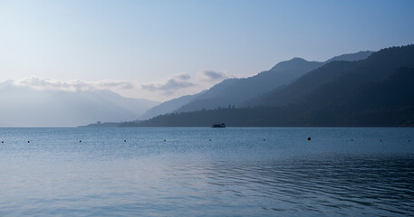 Blue mist shrouds the mountains in morning light, with a blue lake below. Light reflects on the...