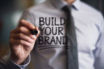 Close-up of hand writing Build Your Brand on a transparent surface, showcasing business concept of brand development and growth, ideal for marketing or advertising campaigns