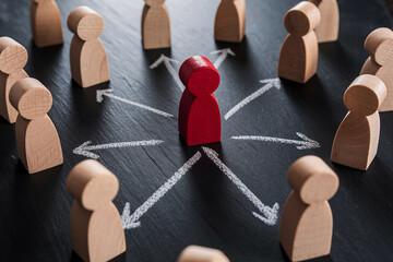 Obraz premium Red wooden figure surrounded by beige figures, arrows drawn on dark surface, showcasing leadership, connection, teamwork, or network concept