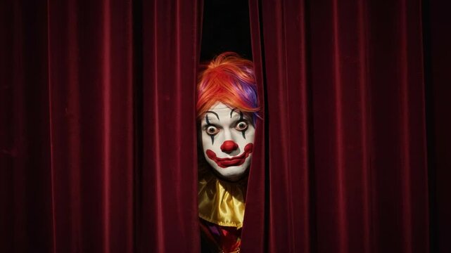 Mysterious clown smiling behind red stage curtains. 4K Video