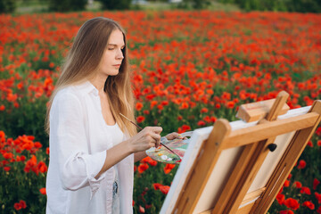 Woman artist painting in poppy field, creating art outdoors