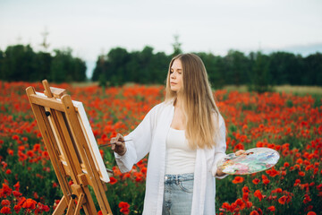 Woman artist painting in poppy field on summer day